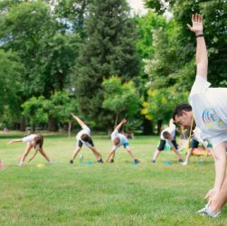 Kids stretching exercises in a park guided by a coach, promoting fitness and fun.