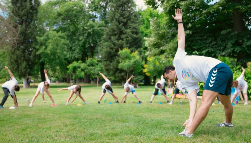 Kids stretching exercises in a park guided by a coach, promoting fitness and fun.